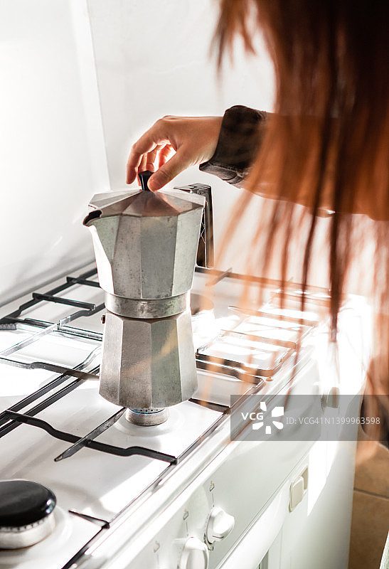 在明亮而阳光充足的厨房里，一个红头发的陌生女人在旧咖啡机里准备咖啡。图片素材