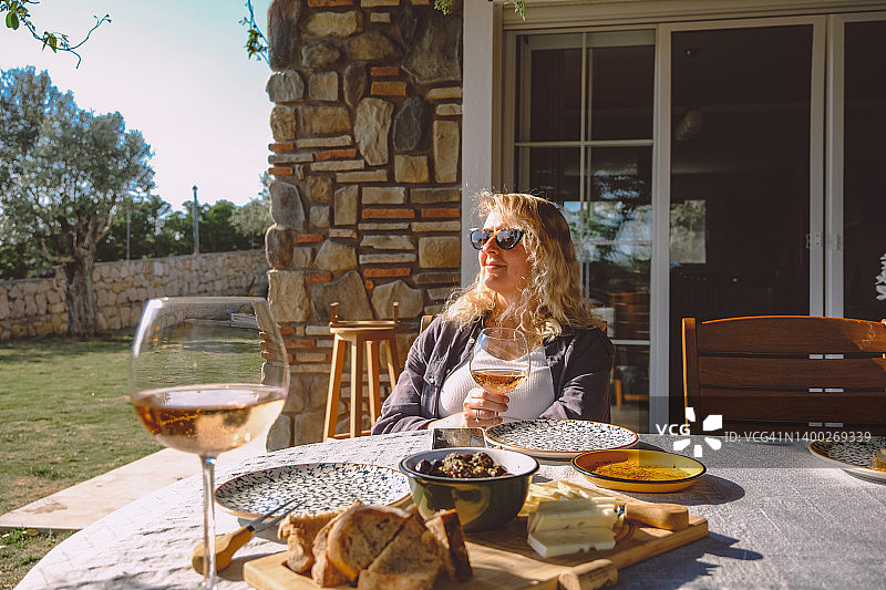 女人坐在外面的桌子上享受一杯葡萄酒。图片素材