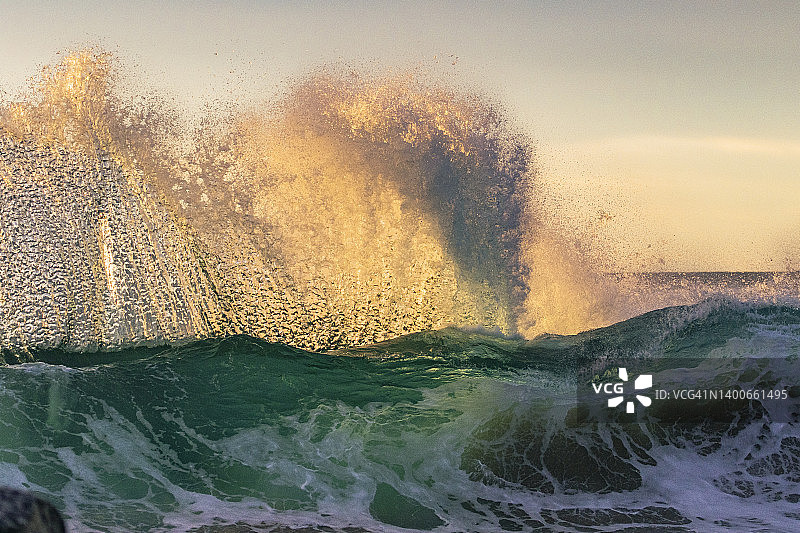 海岸的海浪上升和被明亮的金色的早晨太阳照亮的场景图片素材