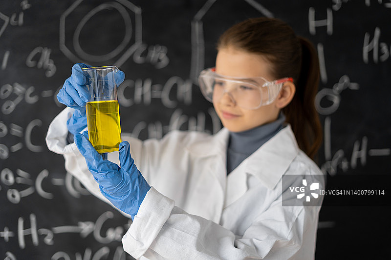 科学家孩子戴着眼镜，穿着实验服带着化学烧瓶，小学生在化学课上在实验室做实验，回到学校的概念图片素材