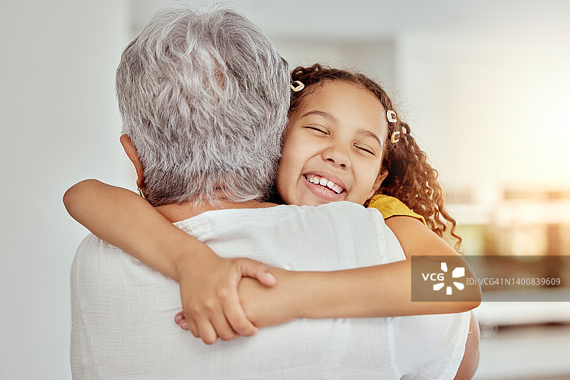 混血的祖母和孙女在家里的客厅拥抱。微笑的西班牙女孩拥抱年长祖父母和在休息室的联系。老人和孩子在一起幸福深情图片素材