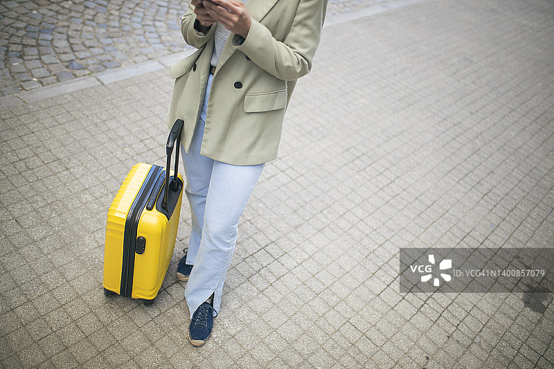 一个不认识的女人刚来度假。她站在街上，旁边是她的黄色手提箱。图片素材