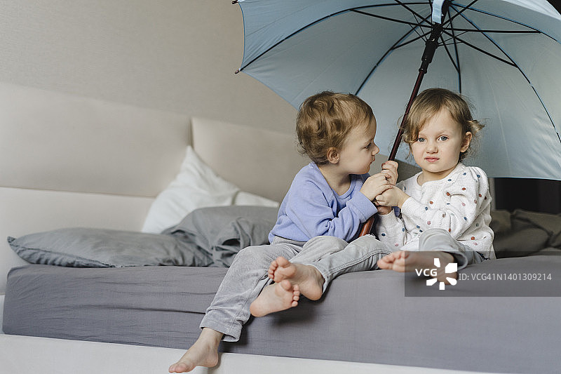 一对双胞胎姐妹撑着伞坐在家里的床上图片素材