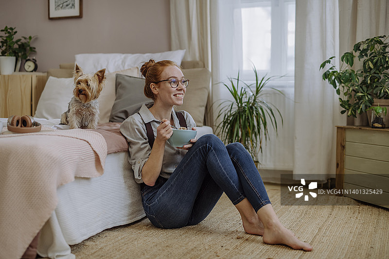 幸福的女人带着一碗食物坐在家里的床上的狗图片素材