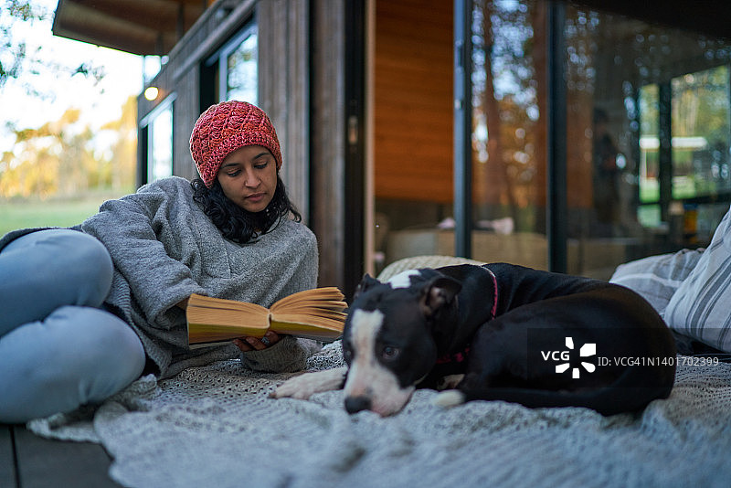 在小屋露台上，女人在狗旁边看书图片素材