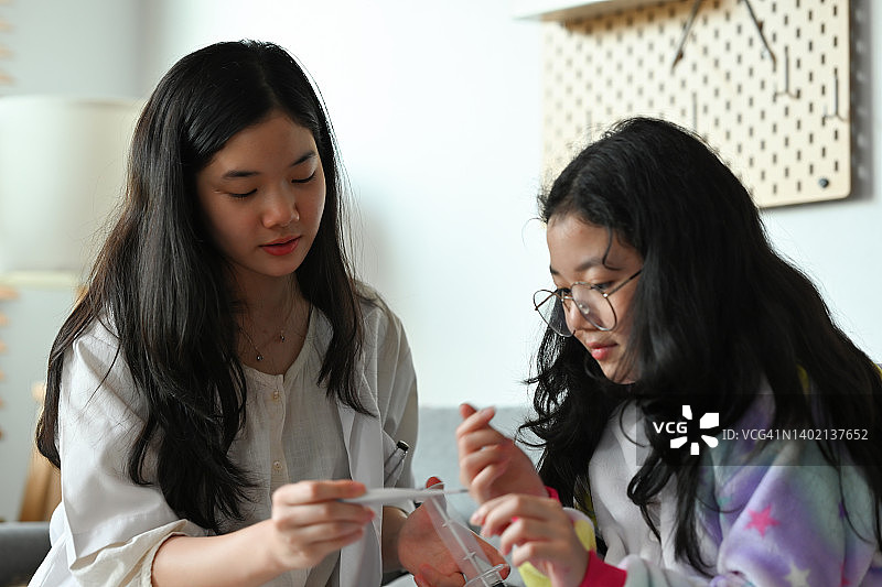 穿着医生外套的可爱的亚洲女孩扮演医生和病人的角色，拿着体温计检查体温，传达教育、事业、健康、家庭的理念。图片素材