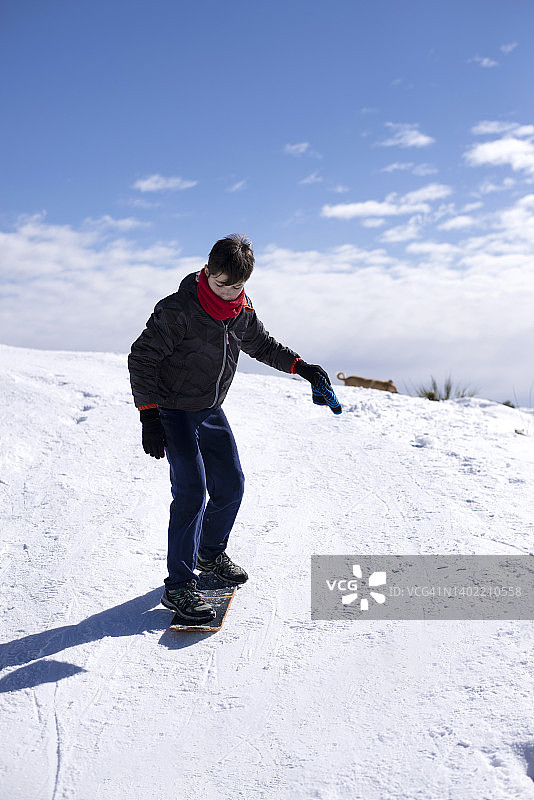 开朗的少年男子在晴朗的霜天骑在雪山上。图片素材