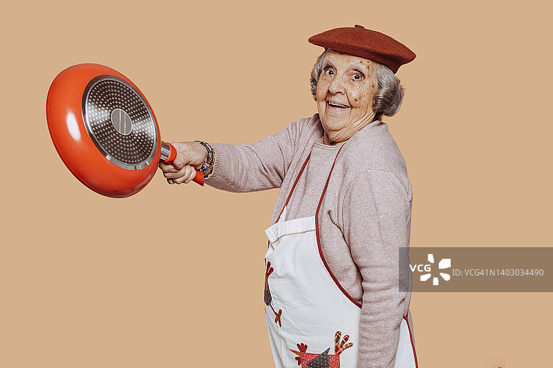 年迈的管家奶奶在工作室拿着煎锅图片素材