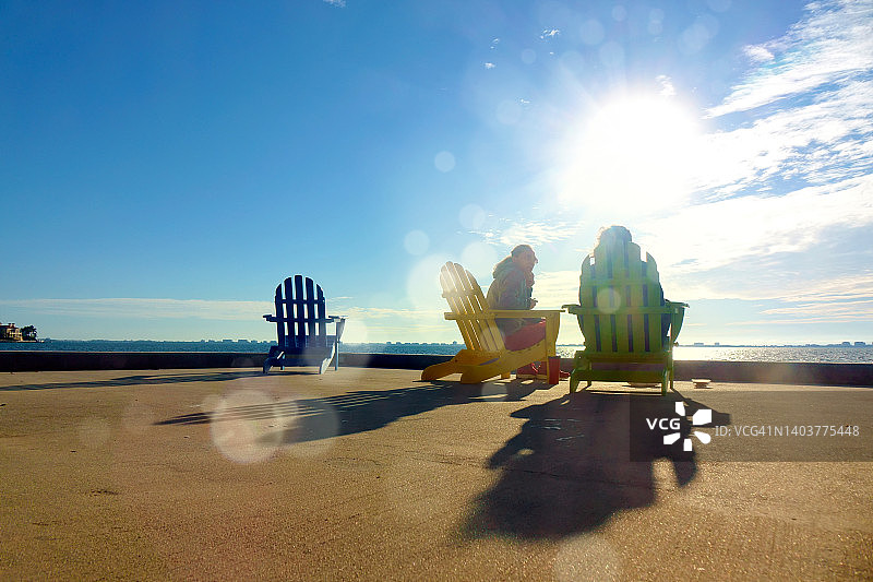 两个女人坐在阿迪朗达克户外椅子上，看着阳光明媚的海景图片素材