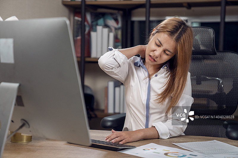 在现代办公室里，年轻的女商人在办公桌前使用电脑时背痛图片素材