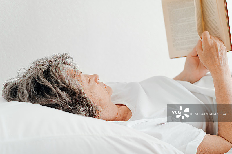 侧视图老年妇女读书，而放松在床上的卧室图片素材