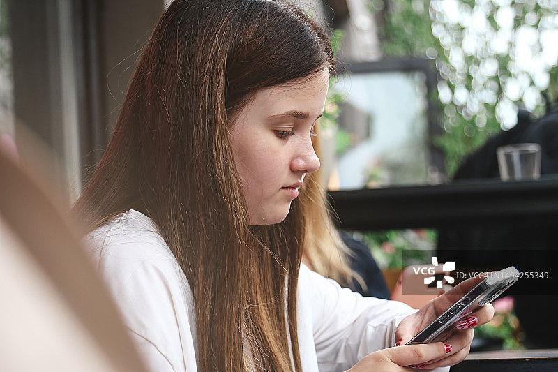美丽的少女长头发坐在路边的咖啡馆和使用智能手机图片素材