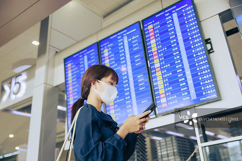 年轻的亚洲女企业家们戴着口罩，在机场的登机牌前阅读电子邮件。商务旅行的概念。图片素材