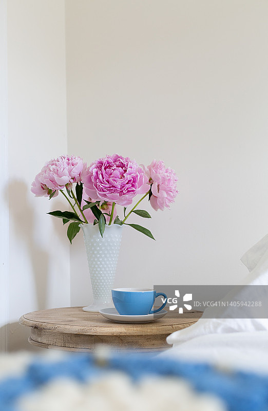 床与钩针阿富汗和木制边桌花瓶的粉红色牡丹和蓝色的一杯茶和文本图片素材