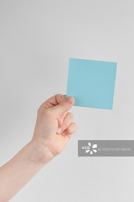 孩子手里拿着一个方形的蓝色空白提示纸或纸条，上面是黑白背景，拷贝空间图片素材