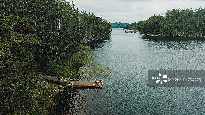 在瑞典森林湖畔的码头上，一个女人和一个男人在思考夏天的风景鸟瞰图图片素材