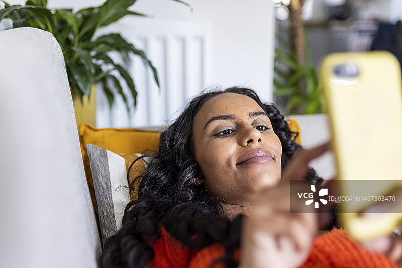微笑的女人放松在沙发上使用智能手机图片素材