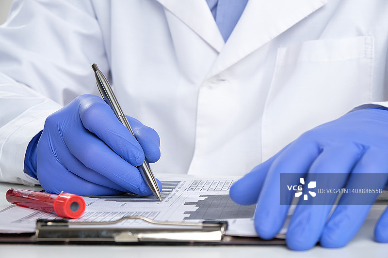 医生或实验室助理填写医疗表格。旁边是一个用于检查的试管。医疗和药品。分析抗体和缺乏的维生素，微量和大量营养素。冠状病毒疫苗的开发图片素材