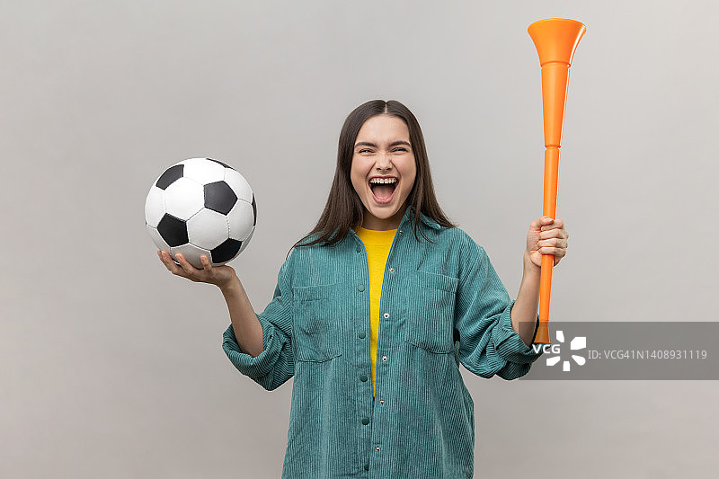 女人拿着扩音器和足球，高兴地尖叫，支持最喜欢的足球队。图片素材