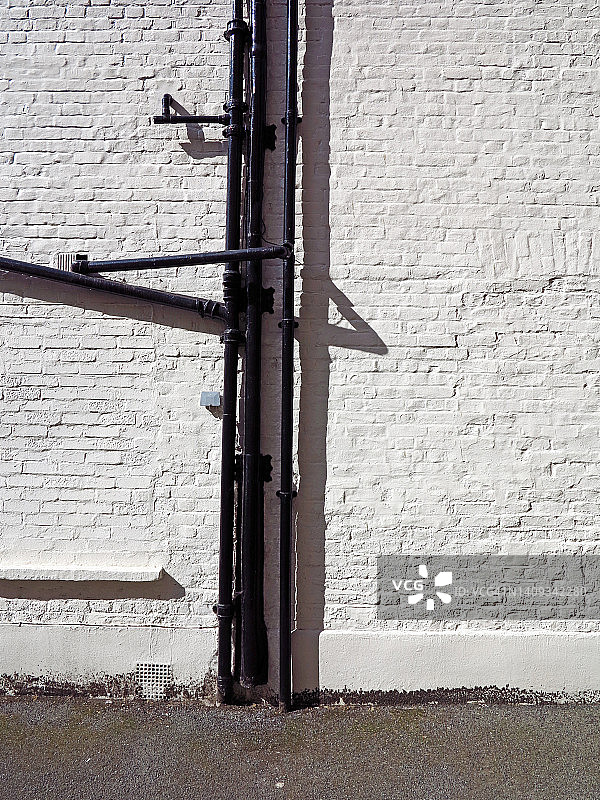 阳光明媚的白色砖墙，黑色金属管道和人行道，英国伦敦图片素材