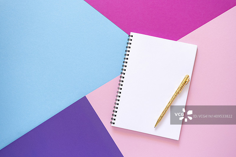 空笔记本与金笔躺在粉红色，紫色，紫色和浅蓝色的纸背景。图片素材