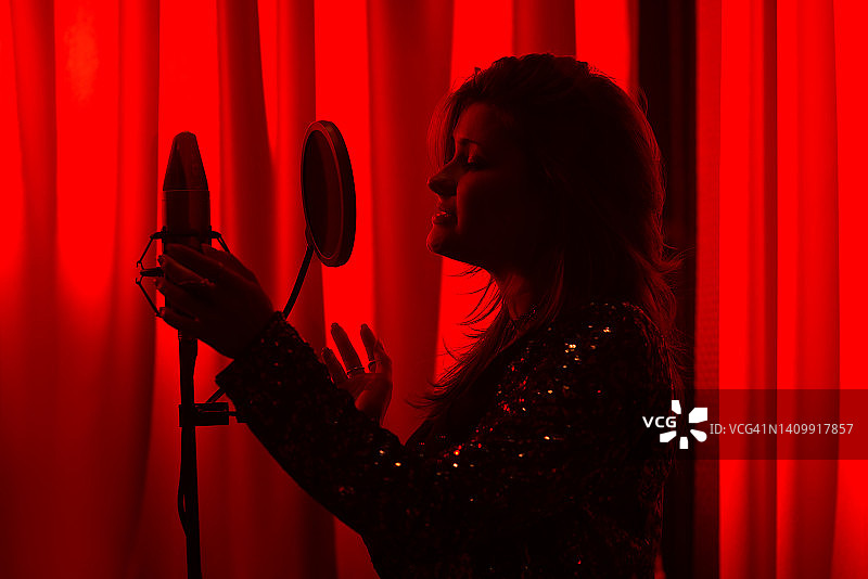 在红色霓虹灯下的录音棚里，女歌手唱歌和录音的剪影图片素材