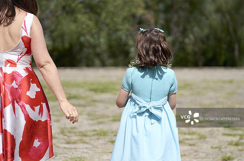 身穿红白相间连衣裙的母亲和8-10岁的女儿从后面拿着一束走路的照片图片素材