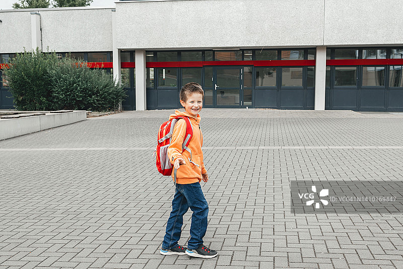 一个背着双肩包的可爱男生站在学校旁边的校园里看着镜头图片素材