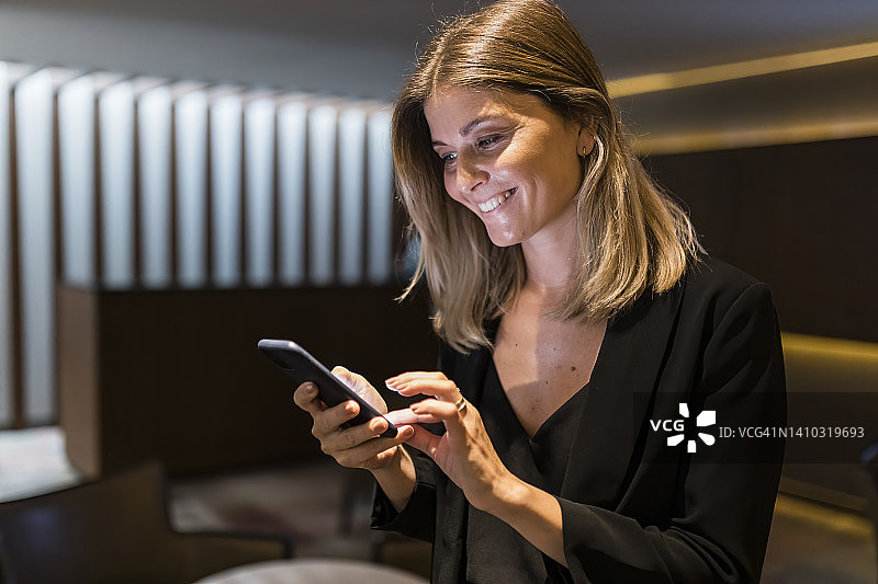 快乐的商人在酒店大堂使用智能手机图片素材