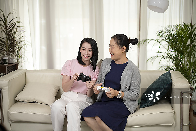 一位年长的母亲和他已经成年的女儿在家里的客厅里一起玩电子游戏。图片素材