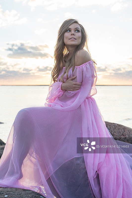 漂亮的女人在日落的时候穿着漂亮的粉色裙子在海滩上图片素材