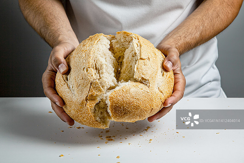 男人们用手掰开用酸面包做的圆形小麦面包图片素材
