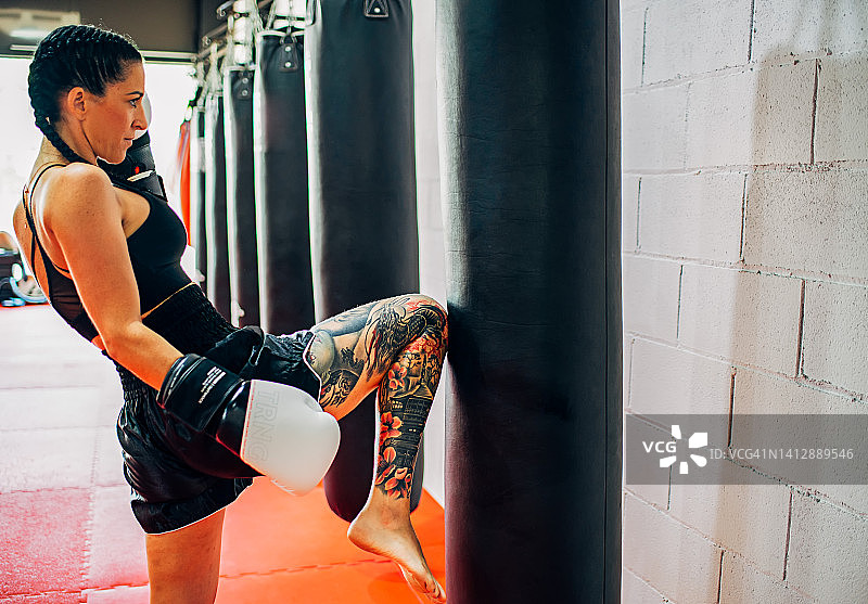 女拳击手练习踢拳与拳袋，有吸引力的女拳击手踢拳袋在健身房的拷贝空间图片素材