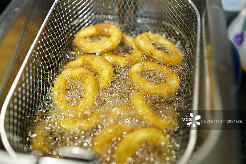 在油炸锅中放入足够的油煎炸鱿鱼甜甜圈，几乎可以把它们捞出来，然后把它们放在吸水纸上，然后吃。图片素材
