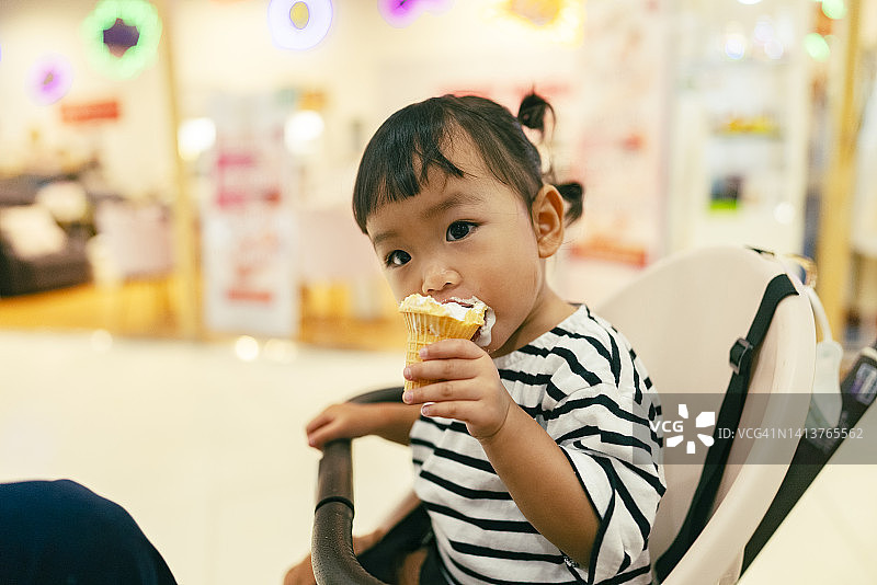 亚洲女婴第一次吃冰淇淋时很开心，嘴里涂满了奶油图片素材