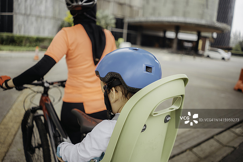 穆斯林妇女骑自行车过马路，她的孩子坐在副驾驶上图片素材