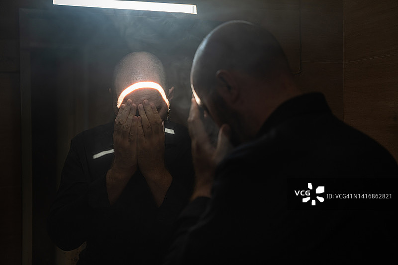 一个男人站在黑暗的房间里，用手捂住自己的脸图片素材
