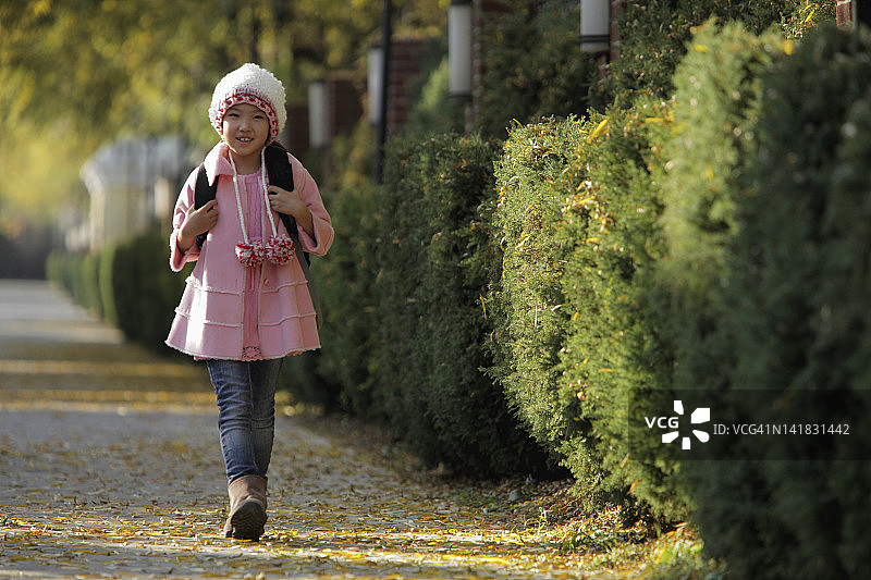 年轻的女孩走在街上，穿着粉红色的外套和帽子，背着背包图片素材