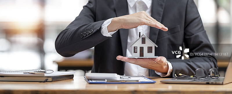 财产保险与保障的概念。商人用双手保护房子的模型、手势和房地产投资者的象征。图片素材