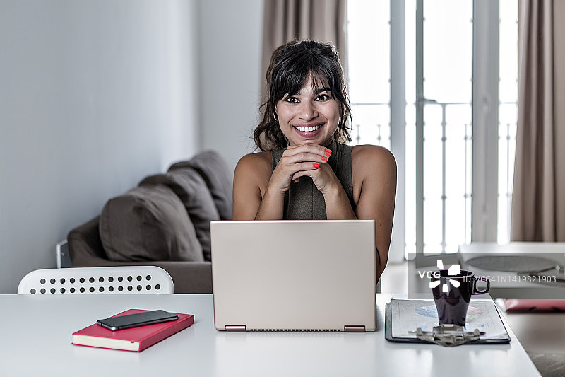 微笑的民族女性自由职业者坐在桌子与上网本在远程工作图片素材