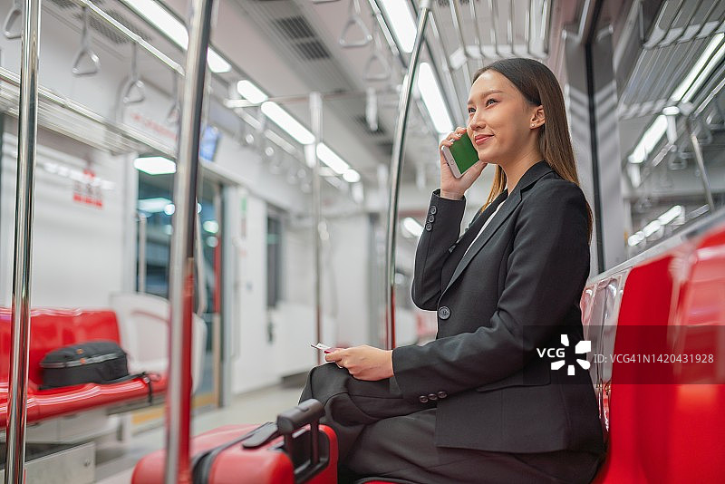 一个年轻的亚洲女商人的肖像照片旅行在通勤火车与她的手机和红色行李去商务旅行图片素材