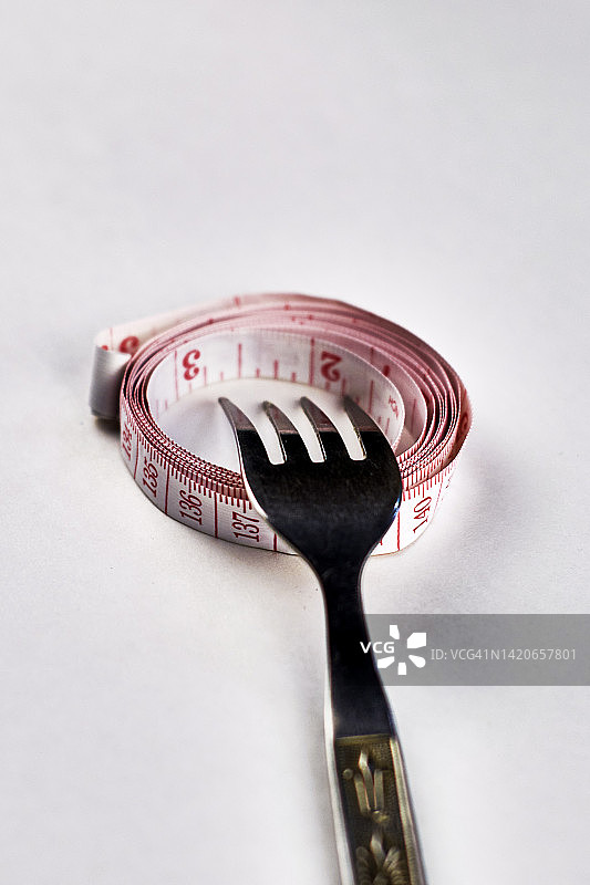 铁叉用卷尺倒绕在白色背景的概念餐盘上图片素材