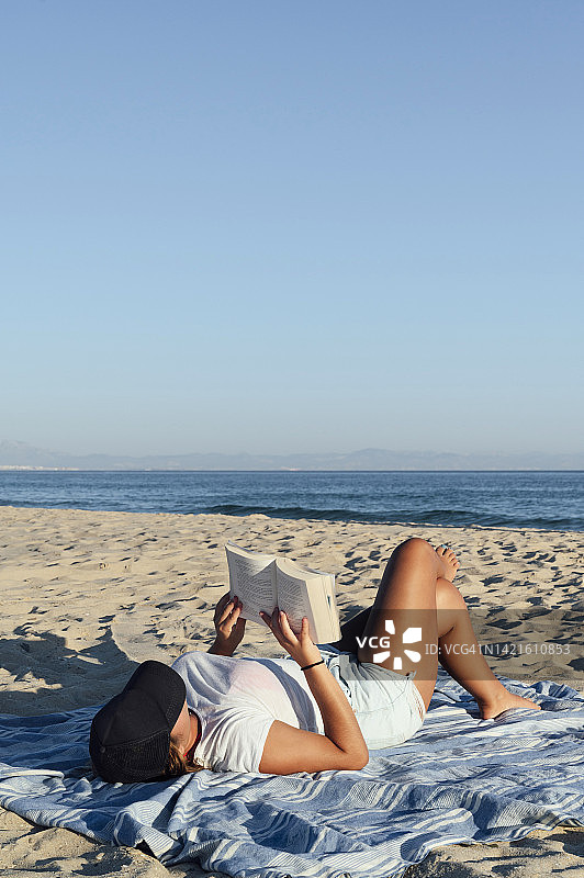 放松的女人在沙滩上翘着腿看书图片素材