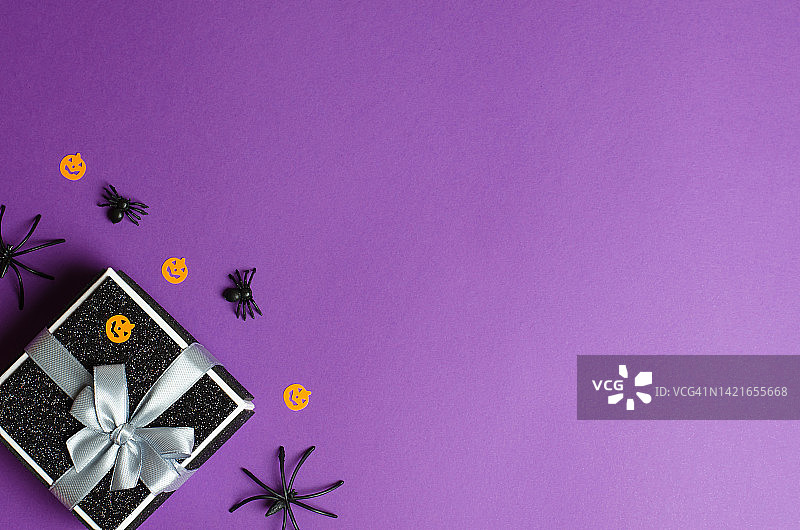 黑色礼品盒和传统万圣节装饰上紫色的背景，拷贝空间。万圣节礼物与促销图片素材