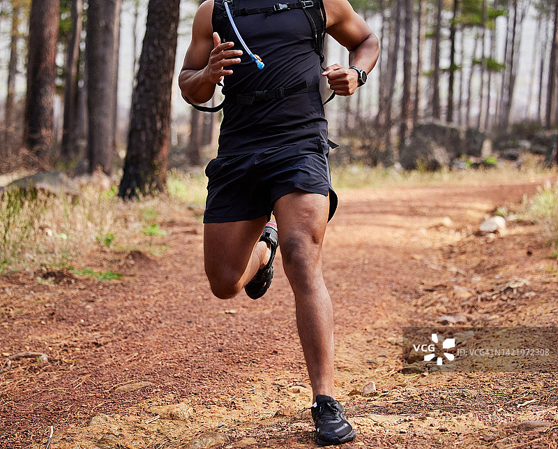 西班牙裔身材健美的男性运动员在野外的森林里跑步。锻炼对健康和幸福有好处。白天一个人在公园慢跑图片素材