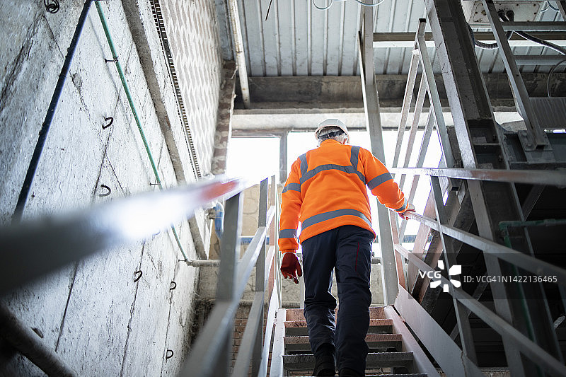 戴安全帽和安全帽的工人工程师在工厂爬金属楼梯。图片素材