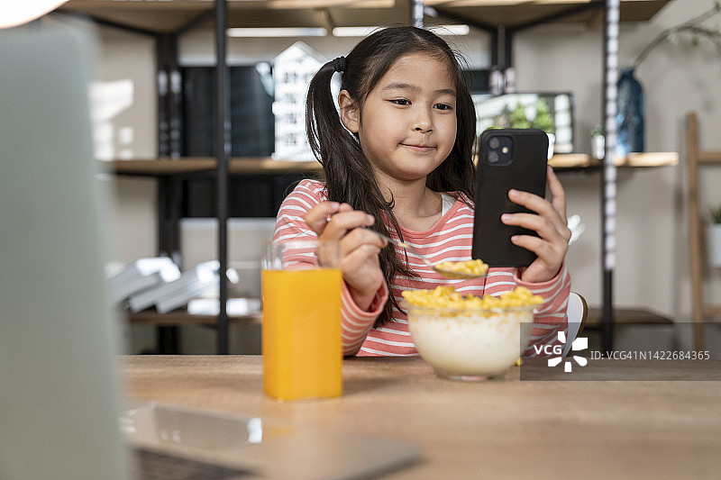 一个小女孩一边吃早餐一边在家上在线课程图片素材
