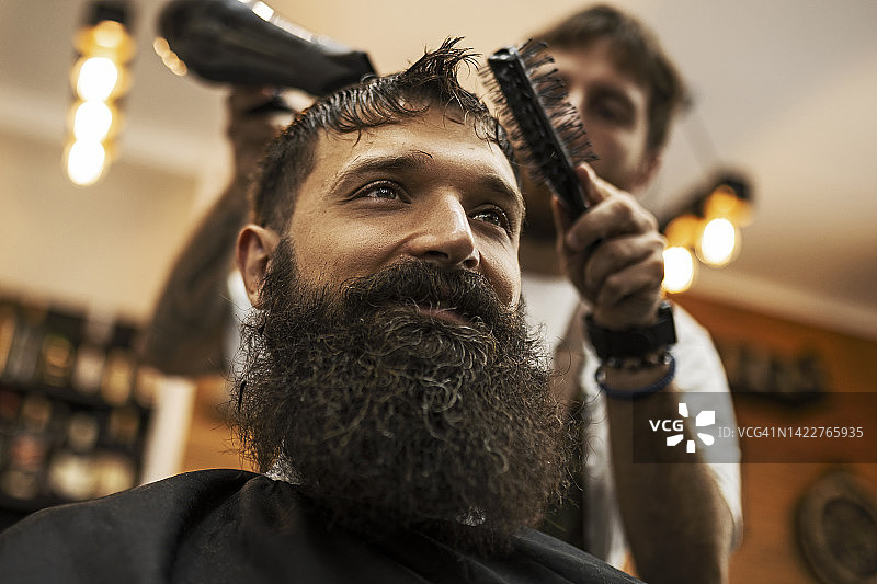 理发师在理发店用吹风机给大胡子理发图片素材