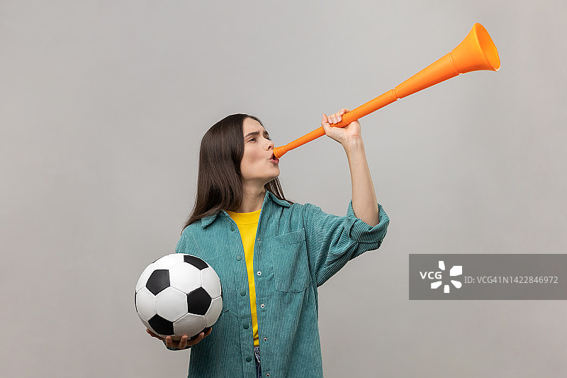 兴奋的女子拿着足球吹着喇叭，庆祝最喜欢的足球队的胜利。图片素材