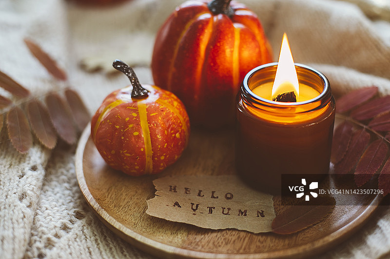 木托盘与燃烧的蜡烛在琥珀罐和两个装饰orabge南瓜。带有文字“你好秋天”的贺卡图片素材